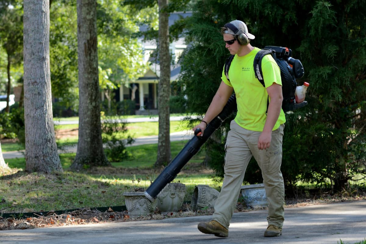 Crew member with a backpack leaf blower cleaning up a residential driveway